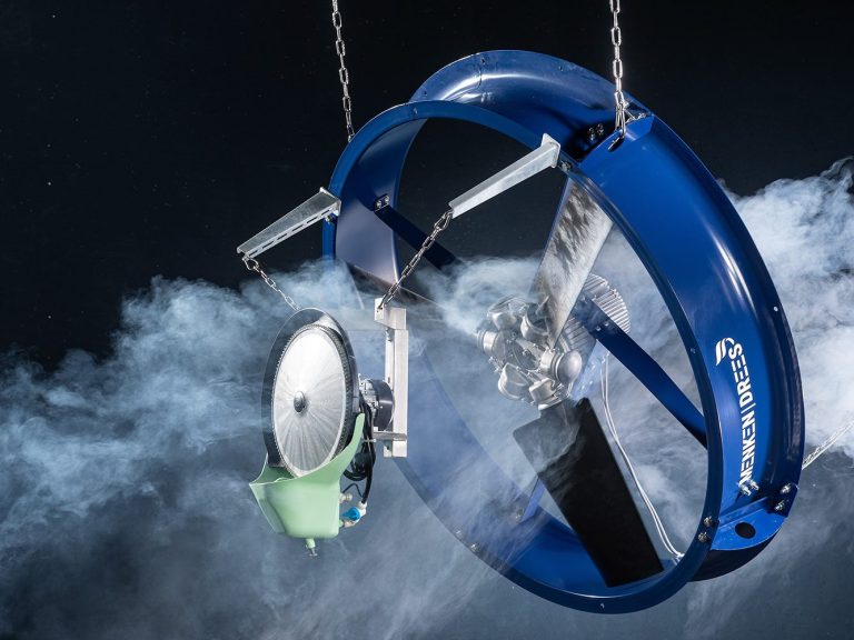 Zwei metallene Stallventilatoren in klein und groß stehen im Lager. Die Regale im Lager sind mit vielen Kartons gefüllt.